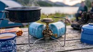 A Campingaz 206 stove with an aluminium windshield set up on a wooden picnic bench at a British campsite.