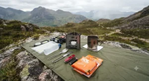 An ultralight hiking kit spread out on a ground sheet featuring the best hexamine stove, spork, pocket knife, and emergency bivvy bag.