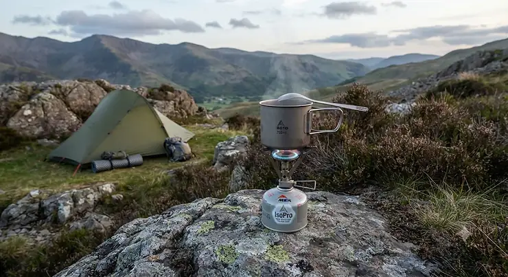 A compact ultralight gas stove set up on a rocky outcrop during a British wild camping trip.