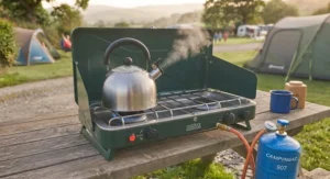 A classic metal kettle boiling on a freestanding double burner camping stove during a weekend camping trip.
