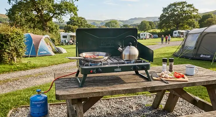 A sturdy freestanding double burner camping stove set up on a picnic table at a British campsite.