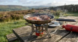 Bacon and sausages frying in a non-stick camping pan over a roaring petrol camping stove during a weekend trip to the Peak District.