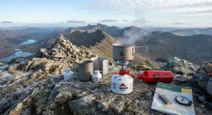 A white gas stove and cooking kit displayed against a backdrop of a British mountain summit.