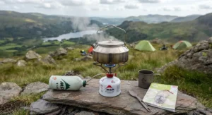 A white gas stove boiling water in a kettle at a scenic British campsite.